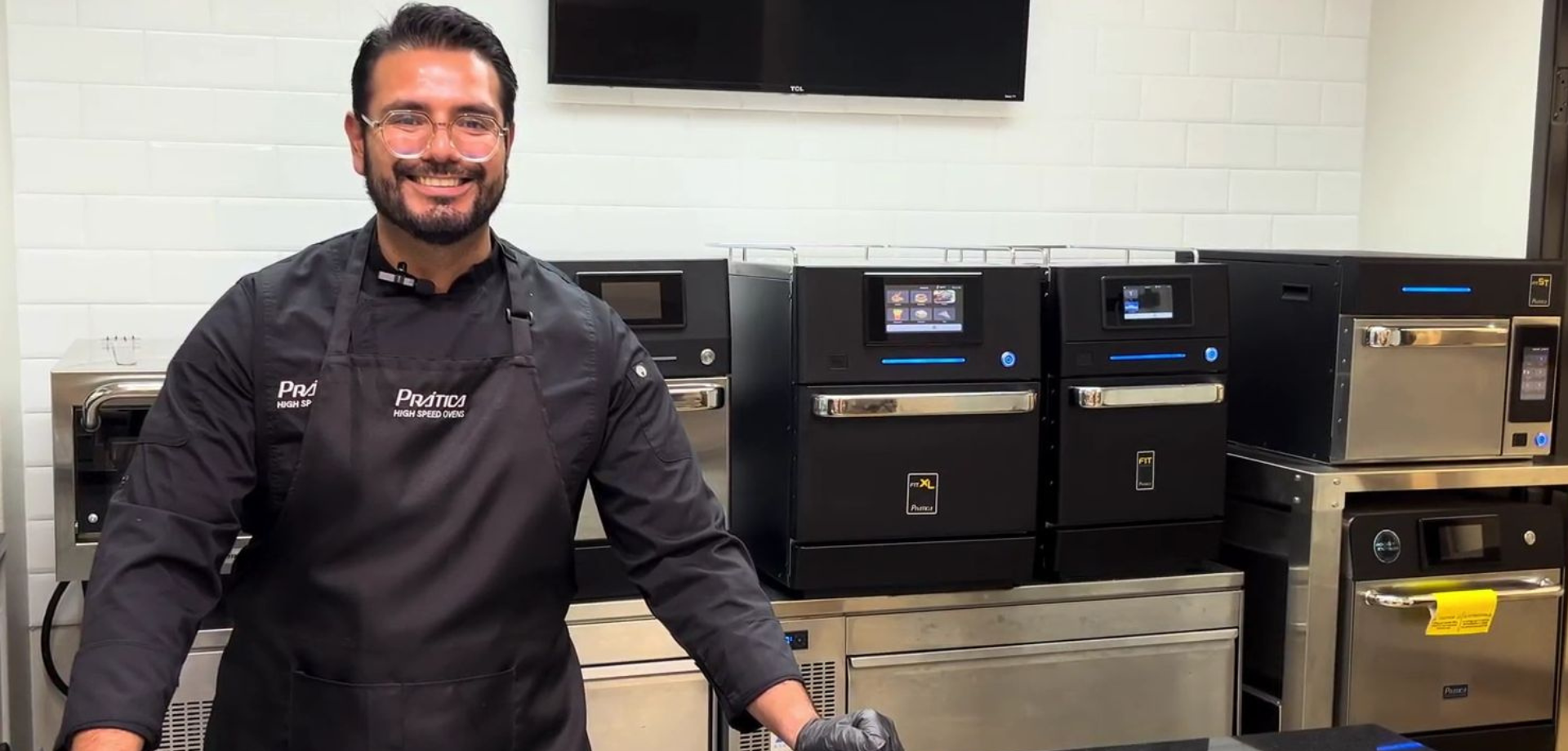 Prática employee smiling in front of Prática high speed commercial ovens.